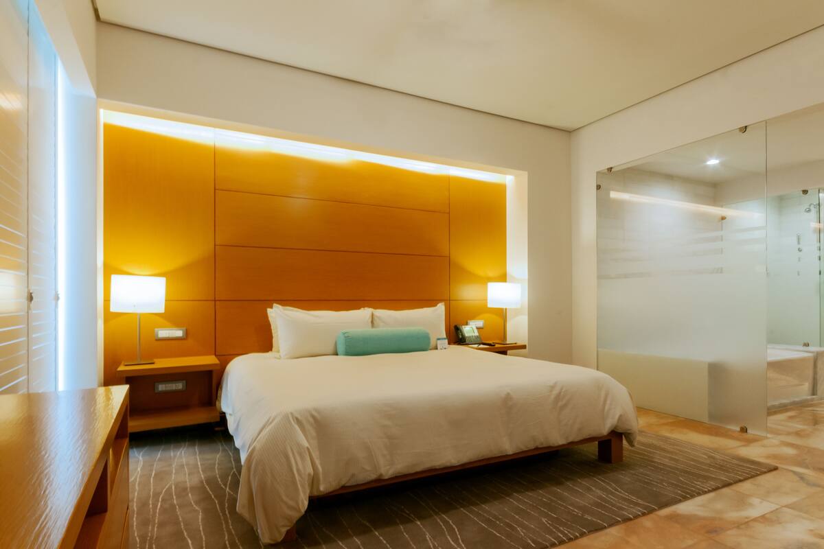 A modern hotel room with a large bed, bedside lamps, a wooden headboard, and a glass shower enclosure.