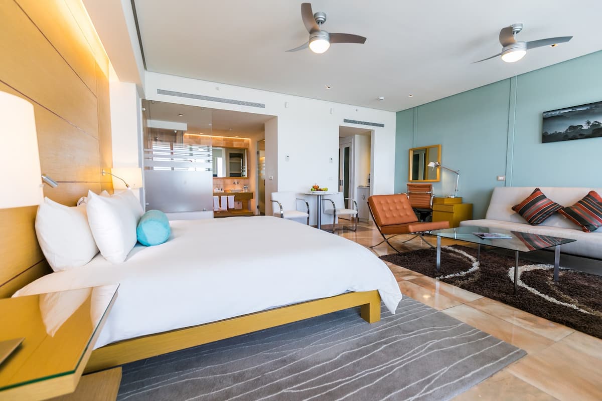 A modern hotel room with a large bed, a sofa, a coffee table, and a dining area.