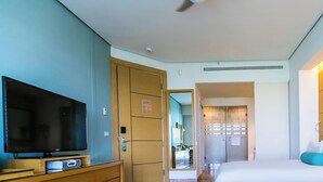 Une chambre d’hôtel équipée d’une télévision à écran plat, d’un lit avec une literie blanche, d’une table de chevet avec une lampe et d’un téléphone.