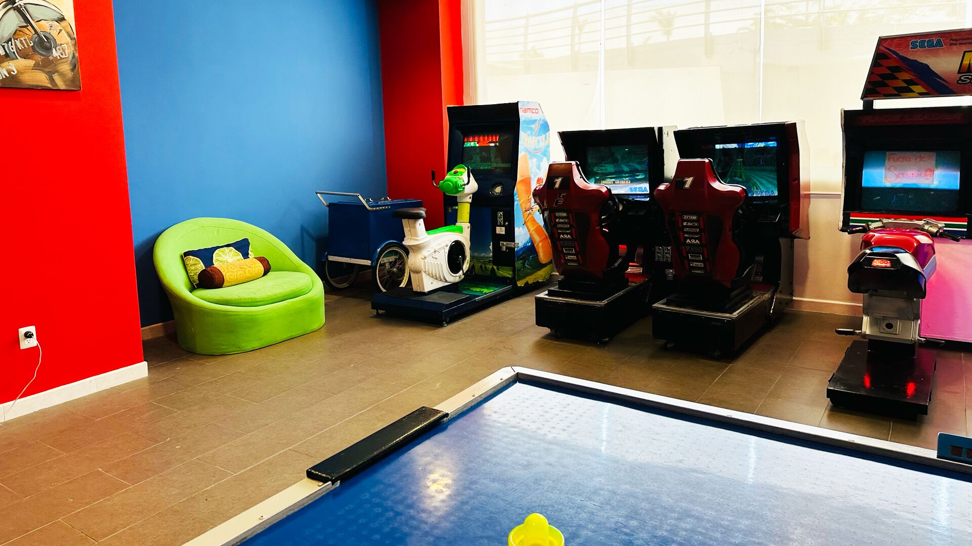A gaming arcade with multiple racing game machines, a green chair, and a table tennis table.