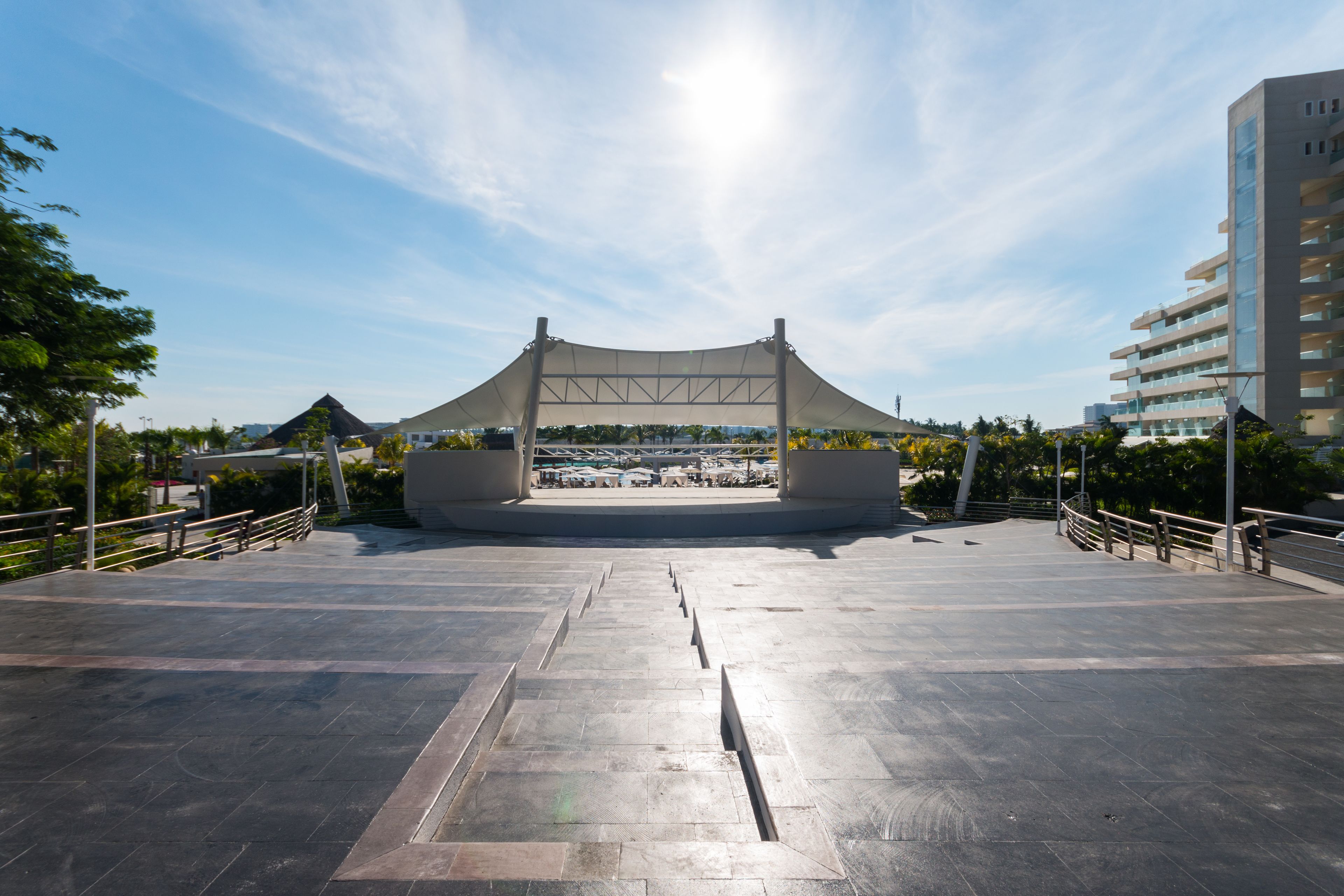 An outdoor amphitheater with a clear view of a beach and a modern building in the background.