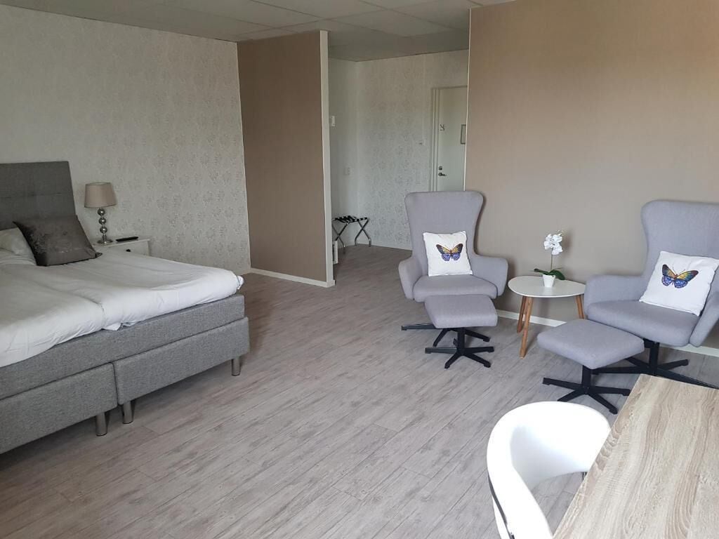 Une chambre d’hôtel avec un lit, deux fauteuils, une petite table et une plante en pot.