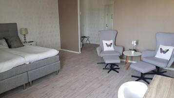 Une chambre d’hôtel avec un lit, deux fauteuils, une petite table et une plante en pot.