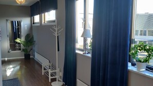 Una habitación con suelo de madera, un perchero blanco, una planta en maceta y una ventana con cortinas azules.