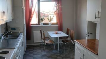 A compact kitchen with a dining area, white cabinets, a window with curtains, and a checkered floor.