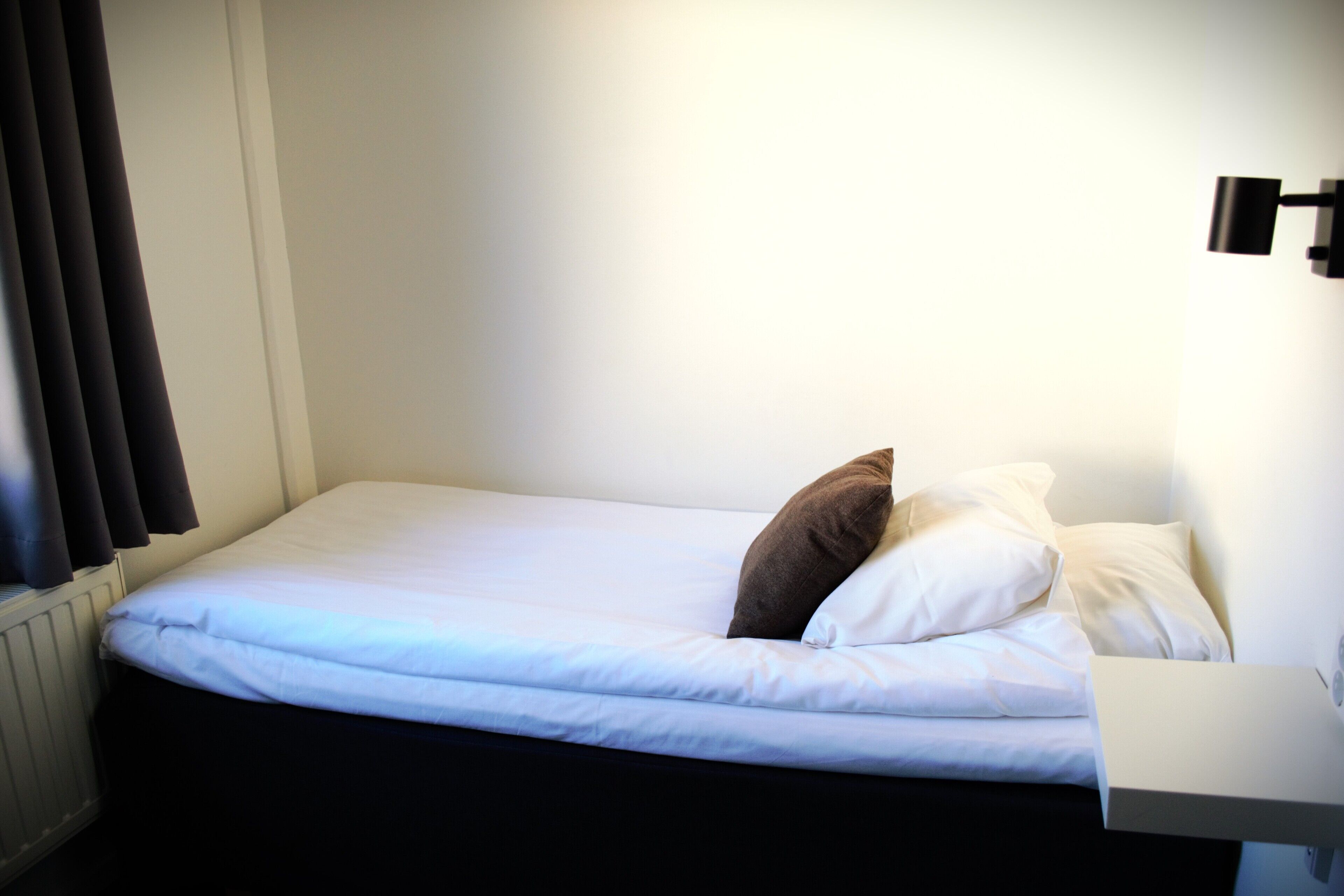 Ein Einzelbett mit weißer Bettwäsche und zwei Kissen, ein Nachttisch und eine Wandleuchte.