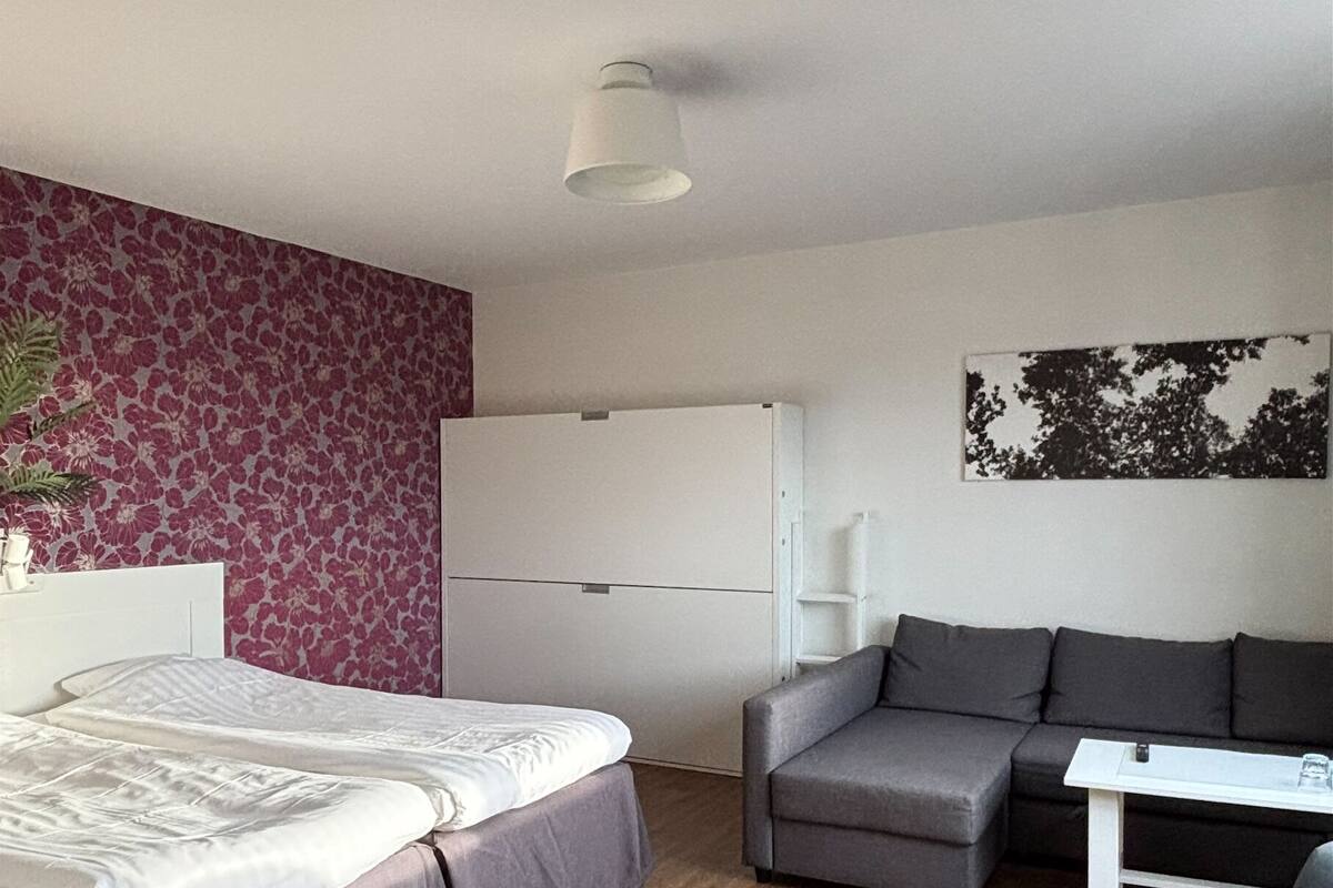 Een moderne hotelkamer met een bed, een grijze bank, een klein tafeltje en een wit kastje.