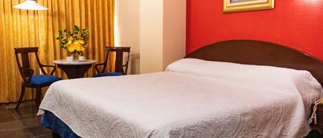 Una habitación de hotel con una cama, una pequeña mesa con sillas, un florero con flores y un cuadro en la pared.