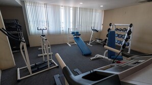 Un gimnasio con equipo de ejercicio, una banca y un estante con mancuernas.