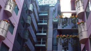 Un atrio de varios niveles con techo de vidrio, varios pisos y balcones con plantas colgantes.