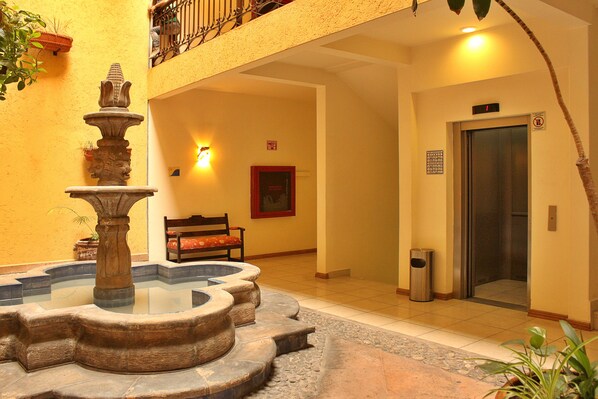 Un patio con una fuente de piedra, un banco, un ascensor y una puerta con un cartel.