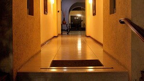 Corredor de hotel com um arco iluminado e acolhedor, piso ladrilhado e quadros nas paredes.