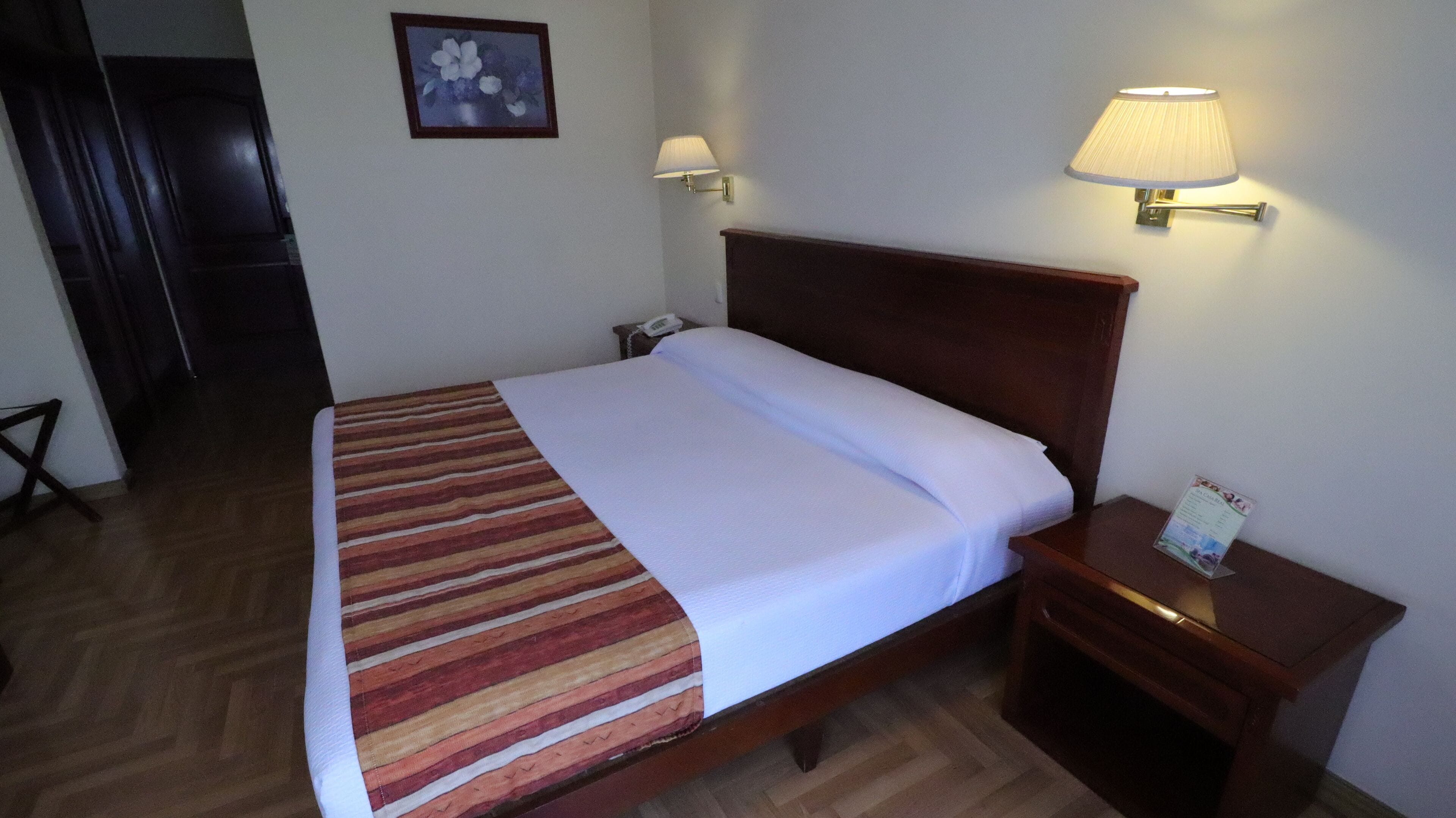 A neatly made bed with a striped blanket, a wooden headboard, two bedside lamps, and a small bedside table with a lamp.