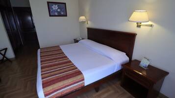 A neatly made bed with a striped blanket, a wooden headboard, two bedside lamps, and a small bedside table with a lamp.