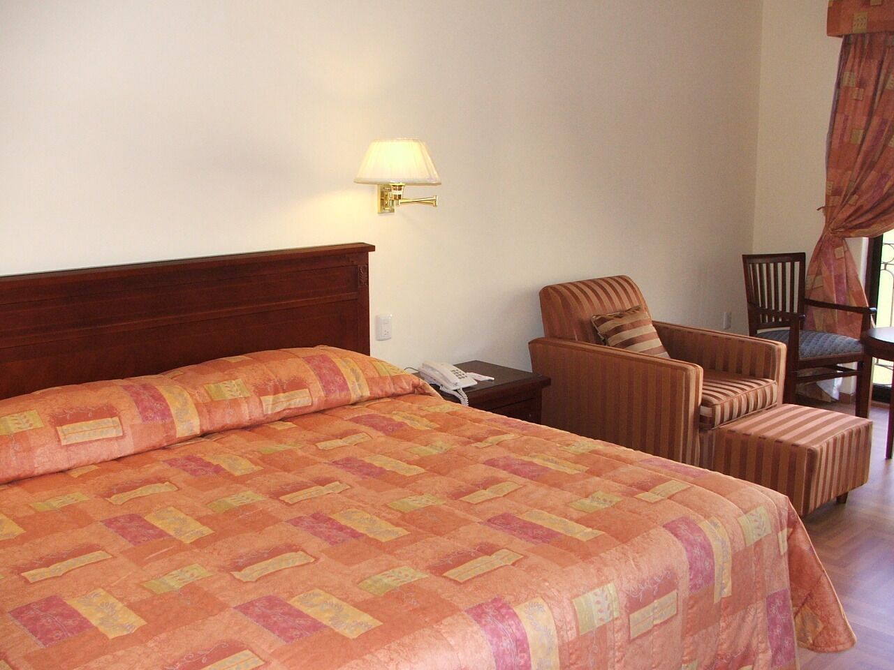 Une chambre d’hôtel avec un grand lit, une table de chevet avec une lampe, un téléphone et deux fauteuils.