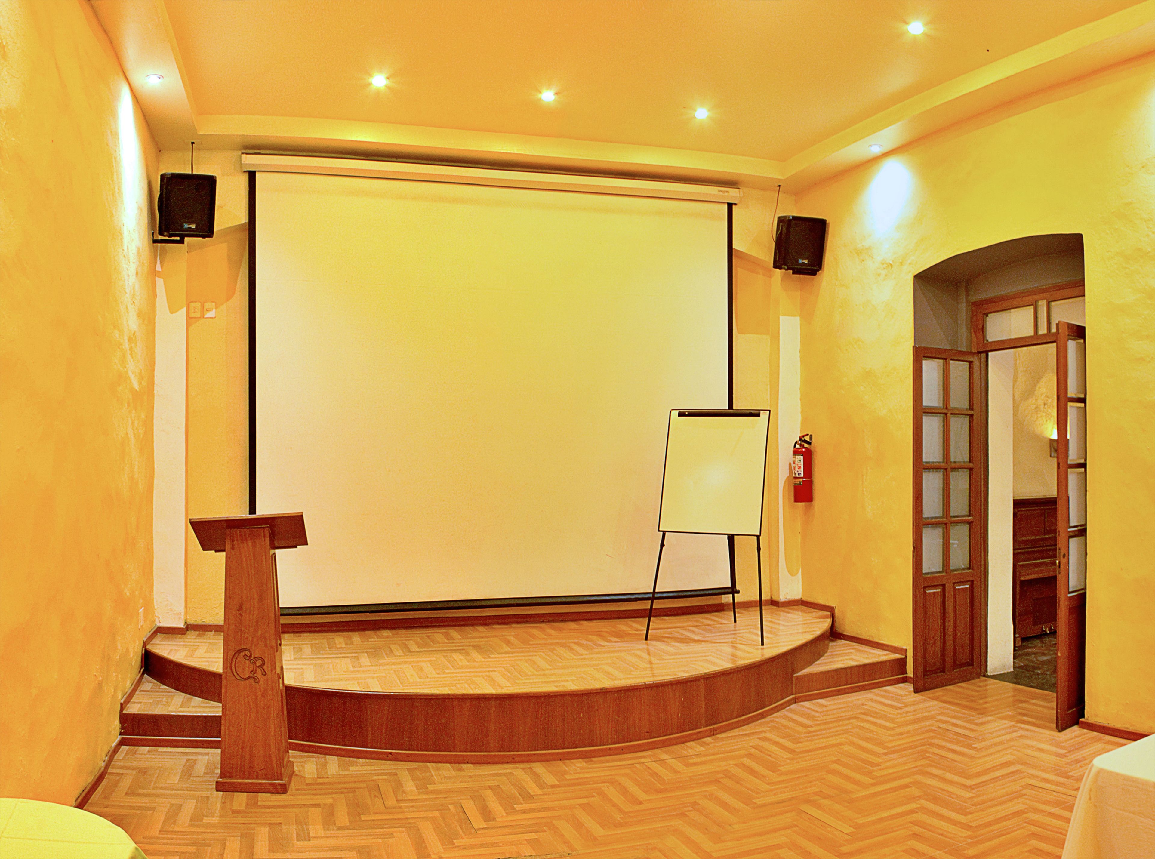 A conference room with a stage, a podium, a projection screen, and a fire extinguisher.