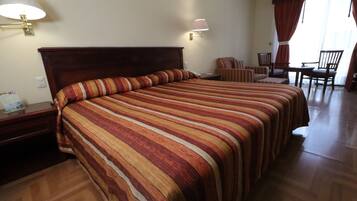 A hotel room with a large bed, two bedside tables, a desk with a chair, and a window with curtains.