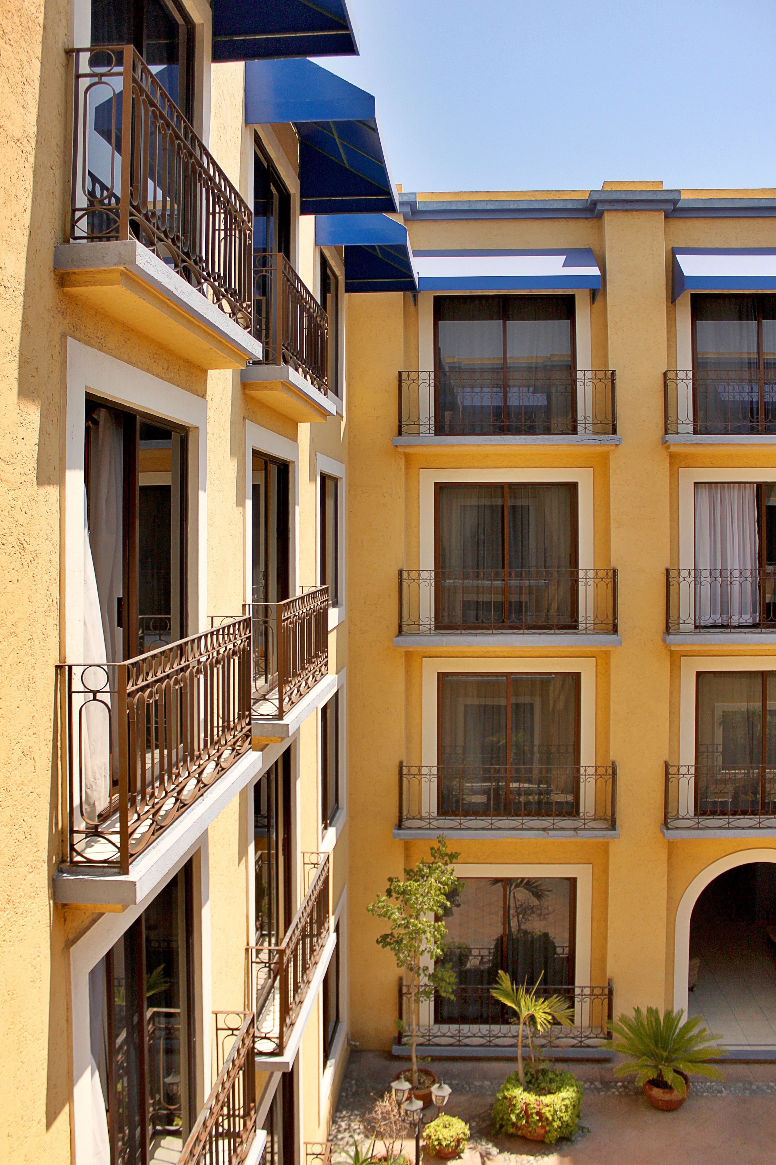 A multi-story hotel with balconies, large windows, and potted plants.