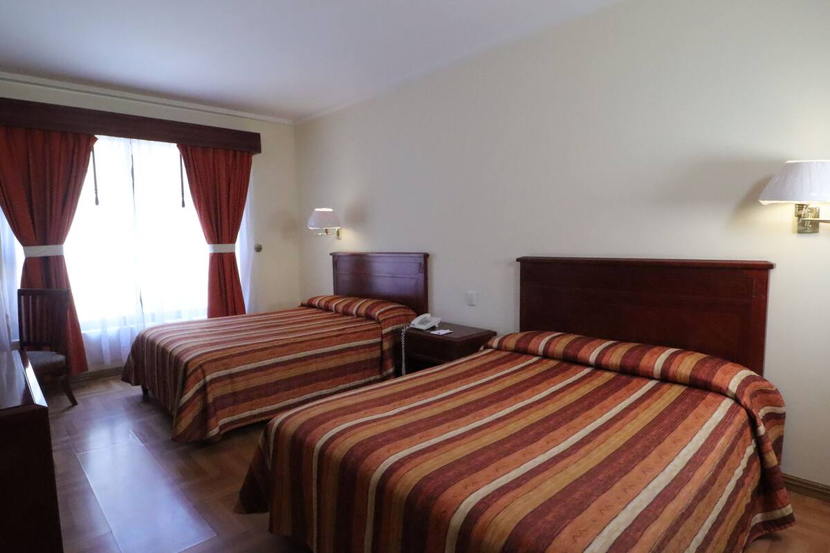 Habitación de hotel con dos camas, un escritorio, un televisor y una lámpara.