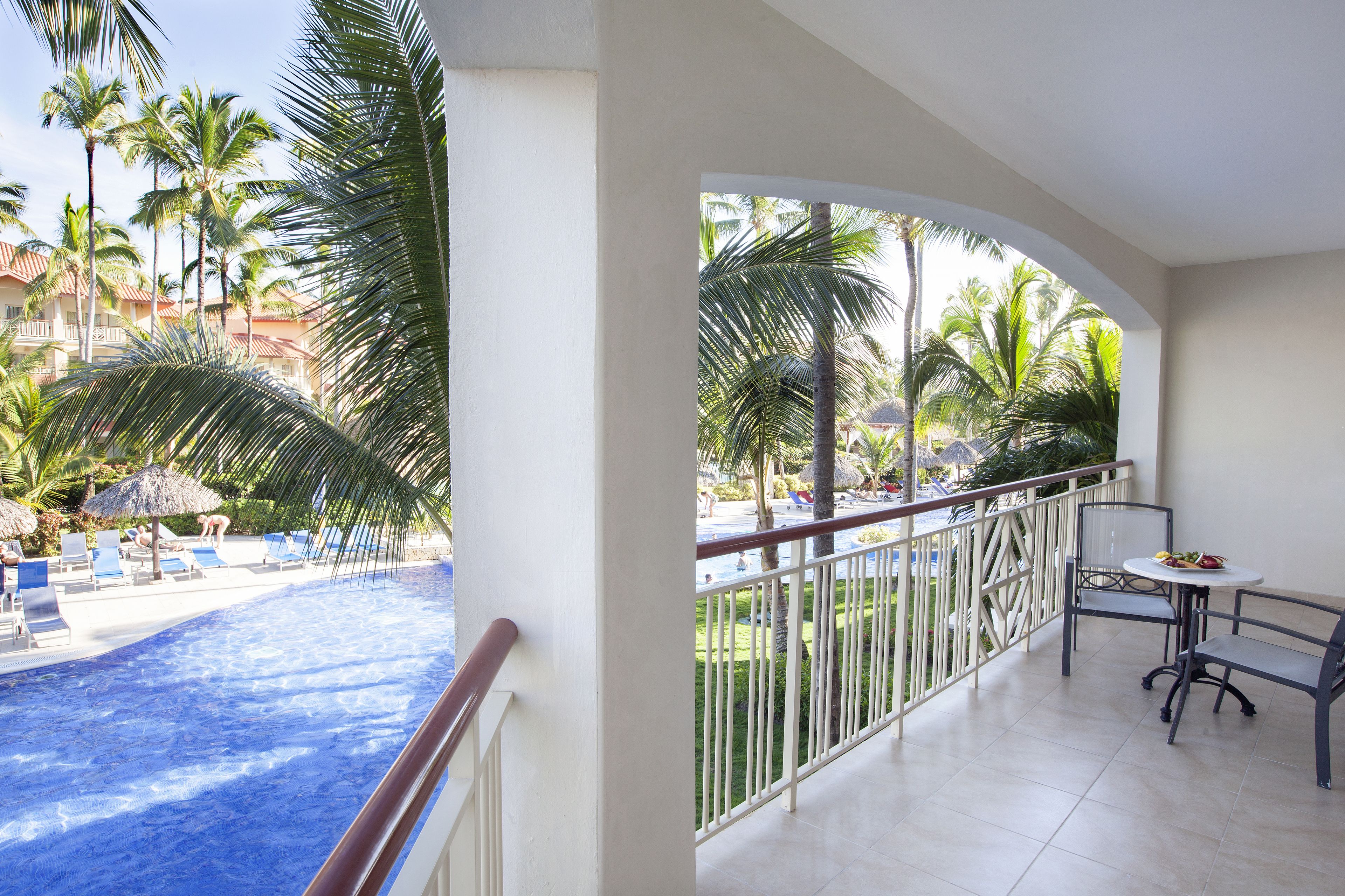 Un balcón con vistas a una piscina, palmeras y sillones de descanso.