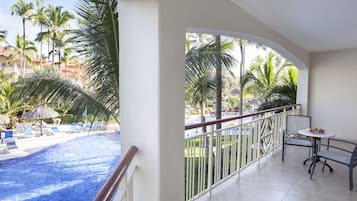 Un balcón con vistas a una piscina, palmeras y sillones de descanso.