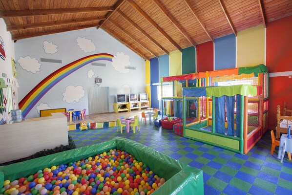 A playroom with a ball pit, colorful play structures, and a rainbow mural on the wall.