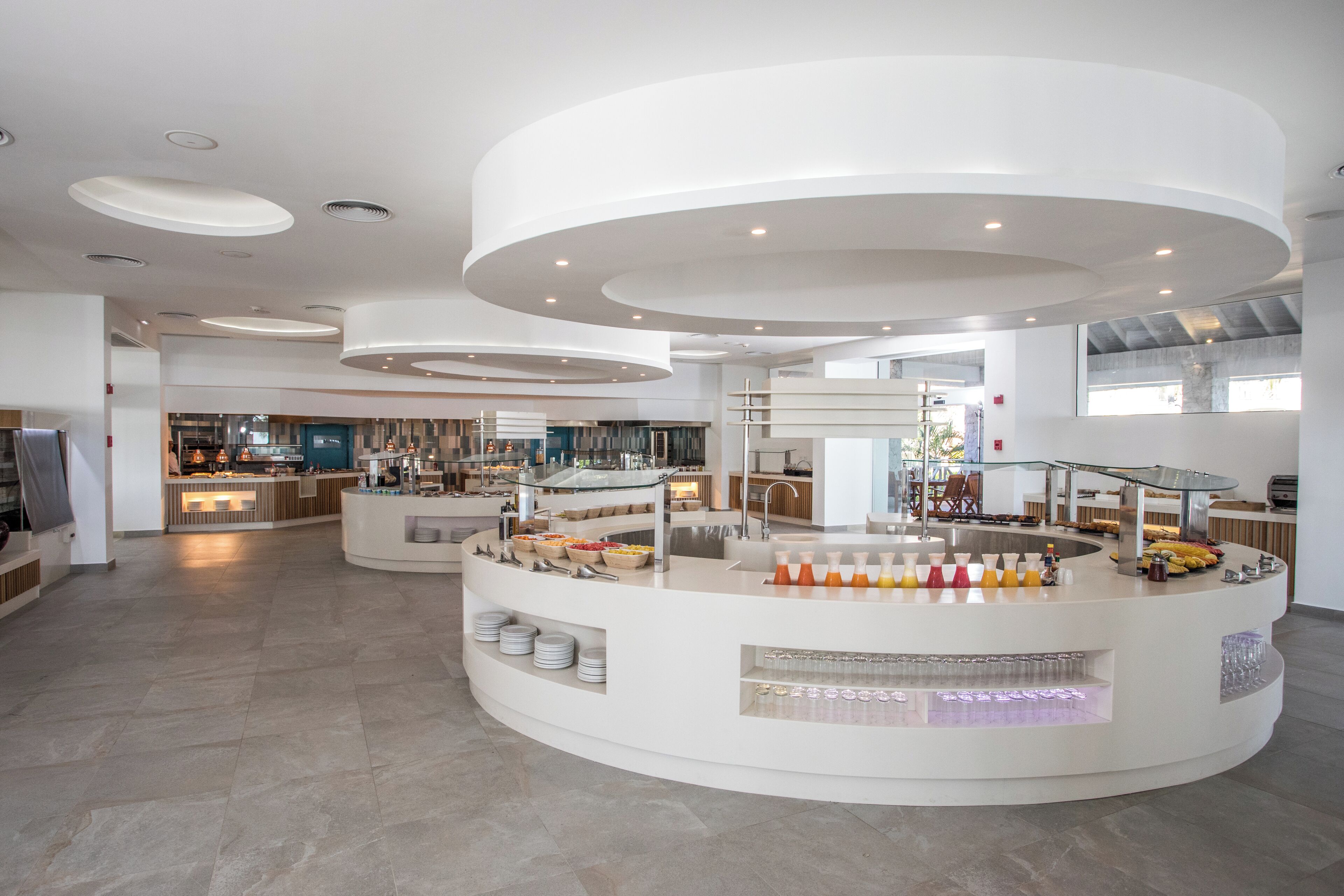 A modern hotel lobby with a central breakfast bar, multiple seating areas, and a spacious layout.