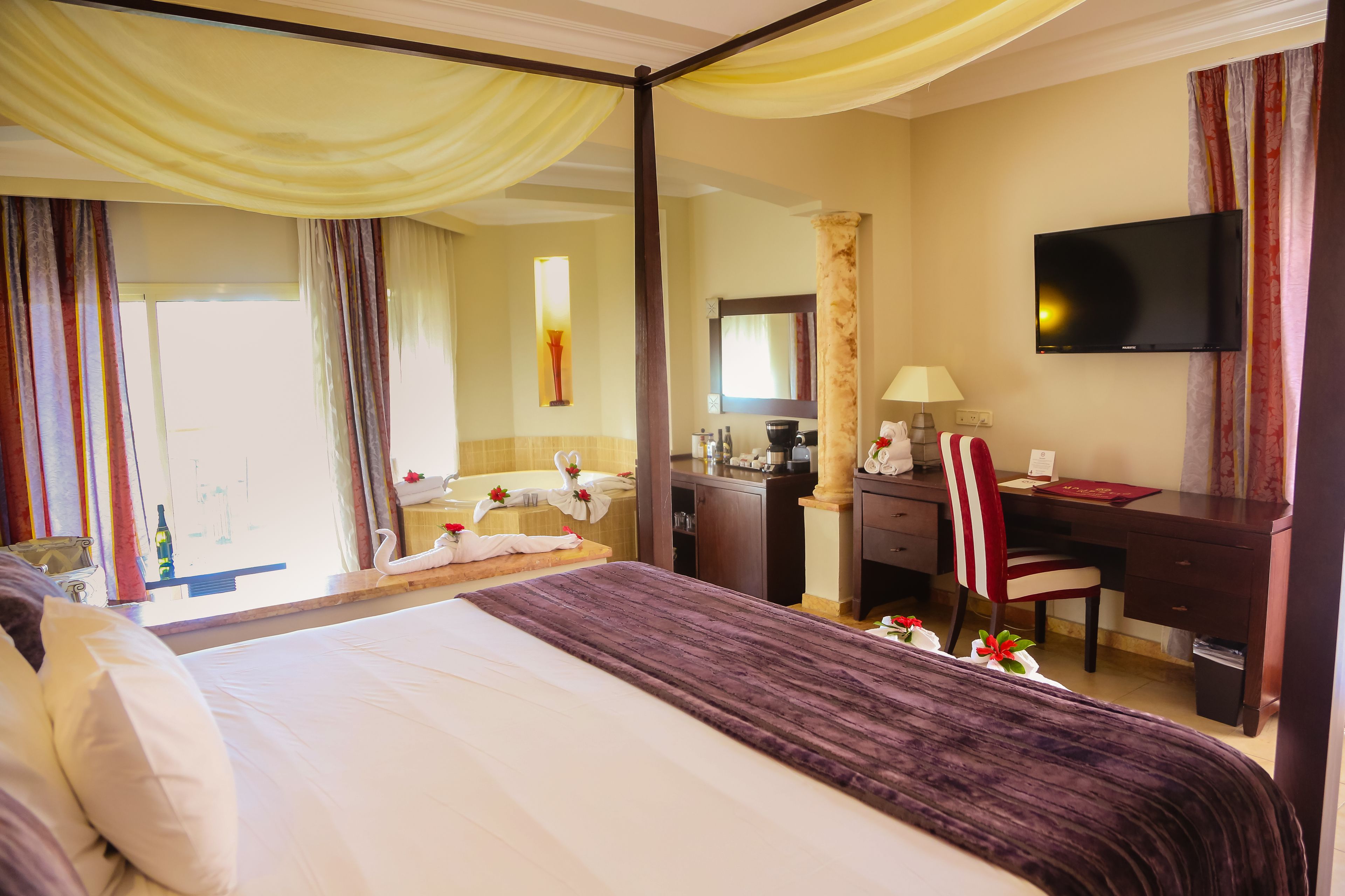 Une chambre d’hôtel avec un grand lit, un bureau, une chaise, une télévision et une salle de bain visible à travers une porte ouverte.