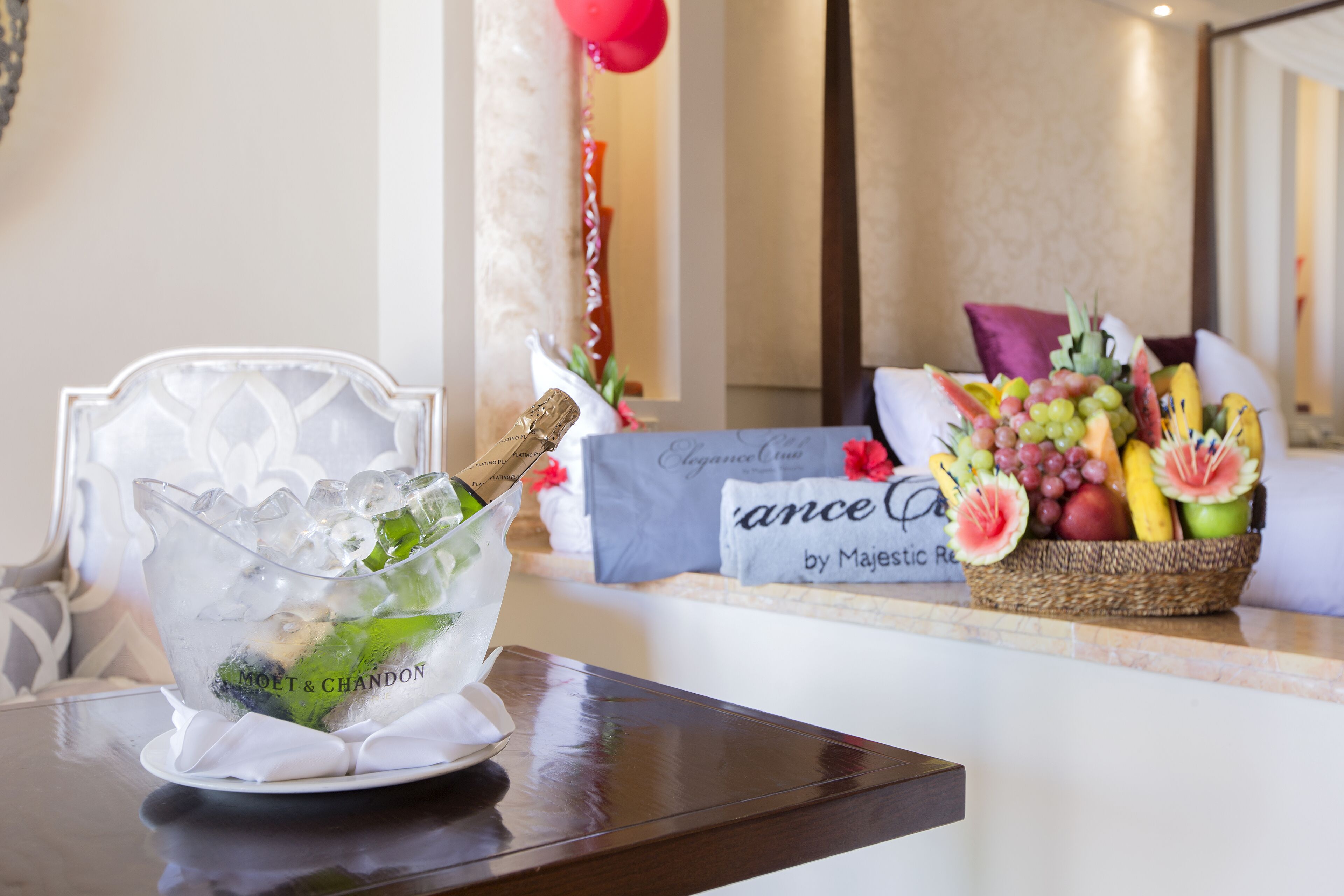 A table with a glass pitcher of champagne, a basket of fruit, and a sign reading "Majestic Retreat."