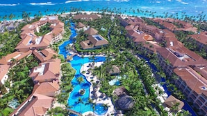 Un resort con varias construcciones, una piscina central y una zona de playa.