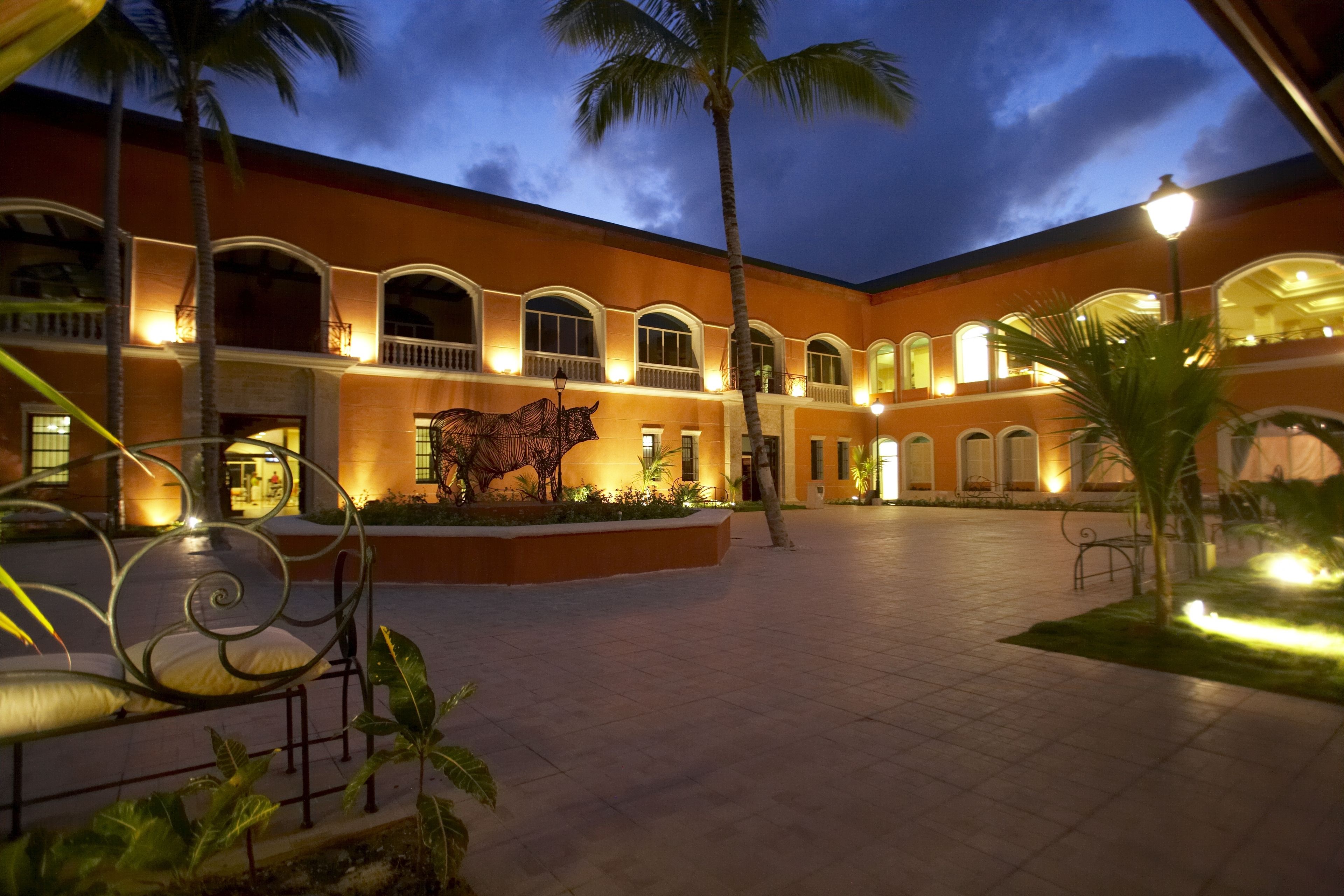 A courtyard with a palm tree, a metal bench, and a building with arched windows and a mural.
