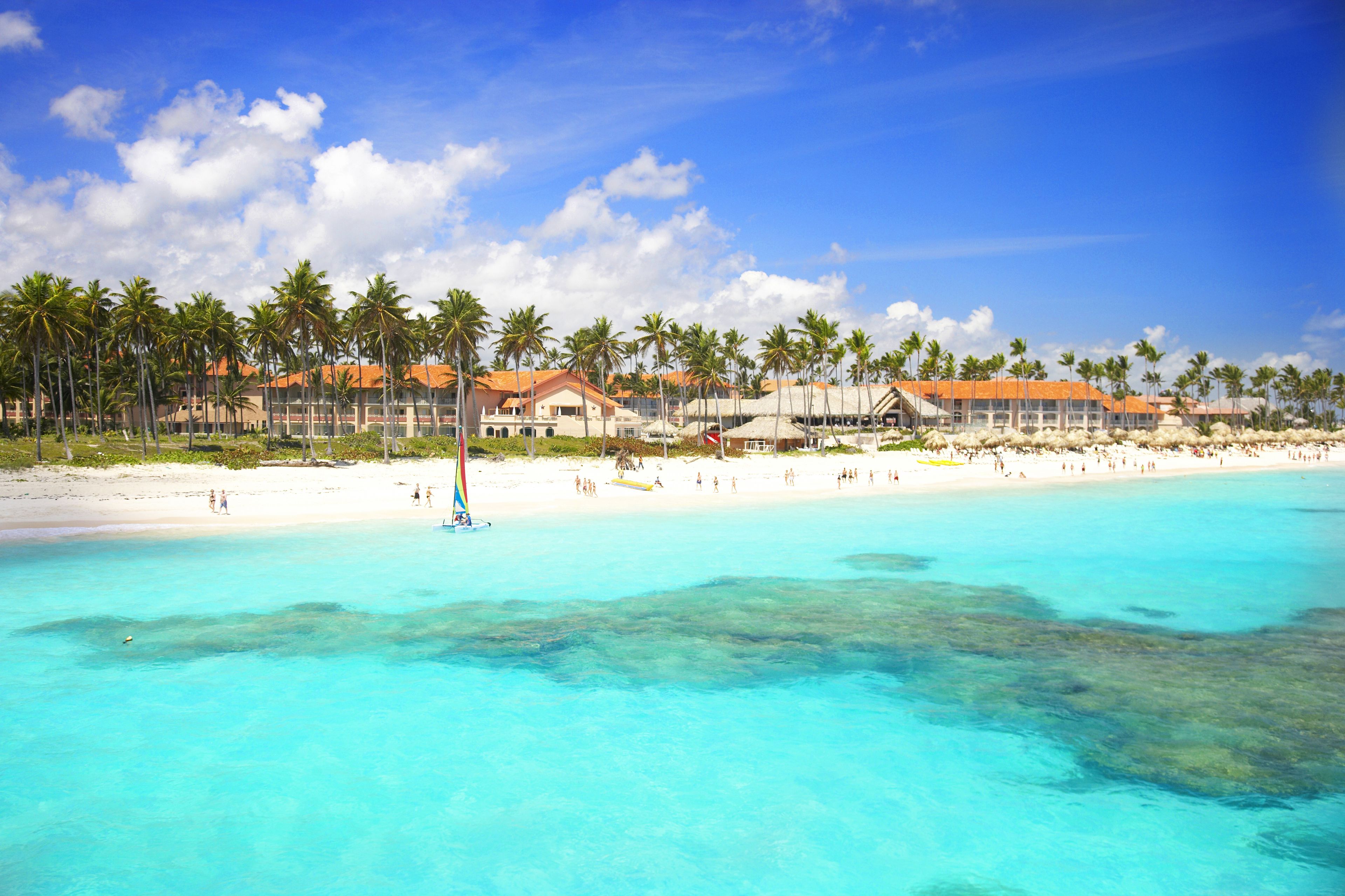 A beach resort with clear turquoise waters, palm trees, and beachgoers.