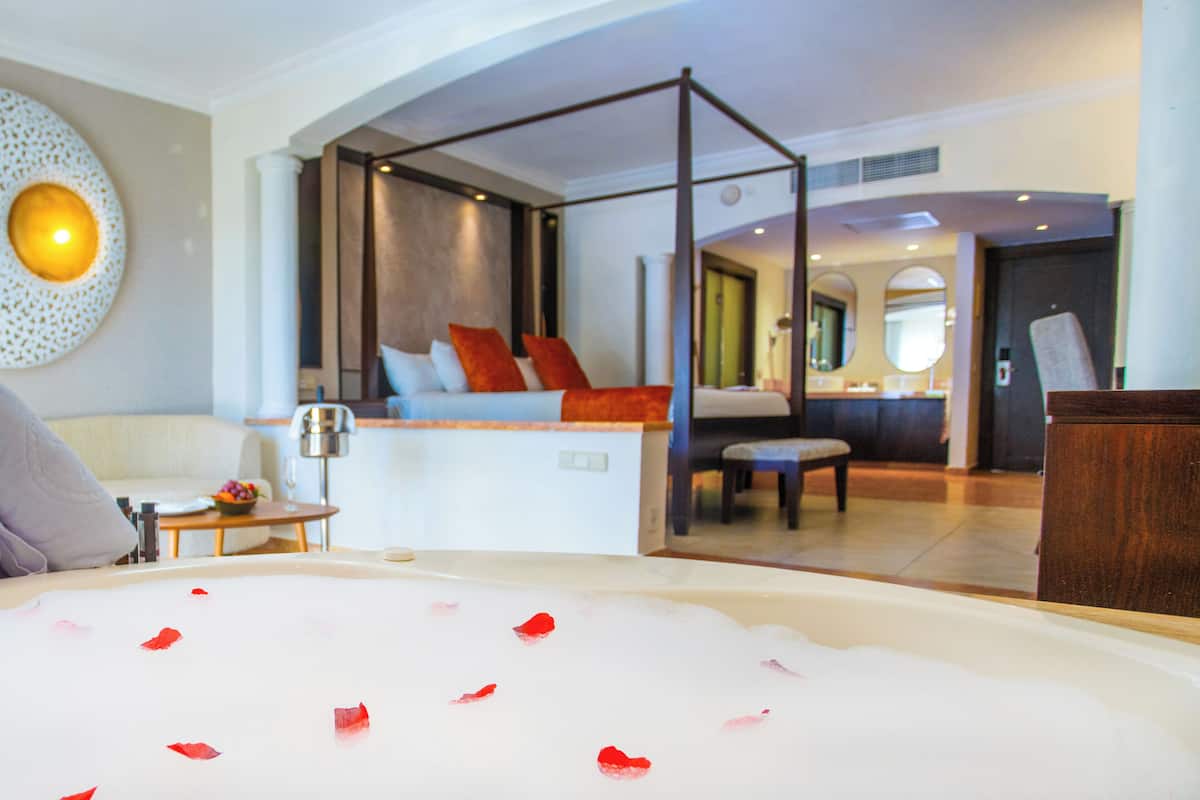 Ein modernes Hotelzimmer mit Himmelbett, einer Sitzecke mit Blick und einem Badezimmer mit Badewanne.