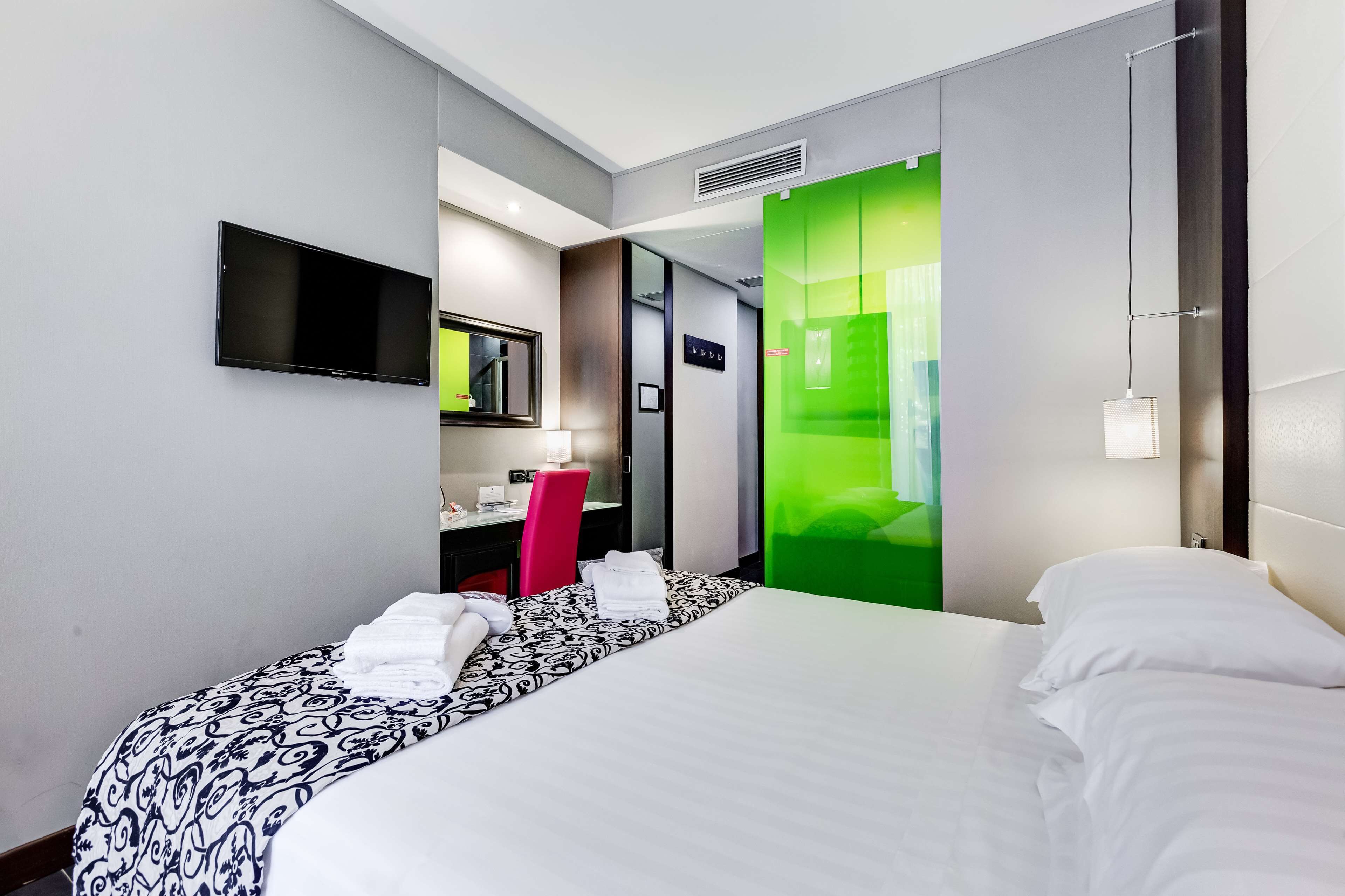 A hotel room with a bed, a desk, a chair, a TV, and a green partition.