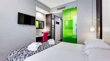 A hotel room with a bed, a desk, a chair, a TV, and a green partition.