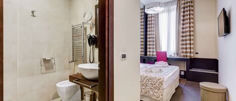 Habitación de hotel con baño, cama, mesita de noche, televisor y ventana con cortinas.