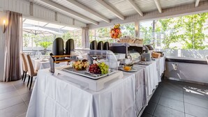 Montaje de bufé con diversos alimentos y una estación de café, bajo un área cubierta con luz natural.