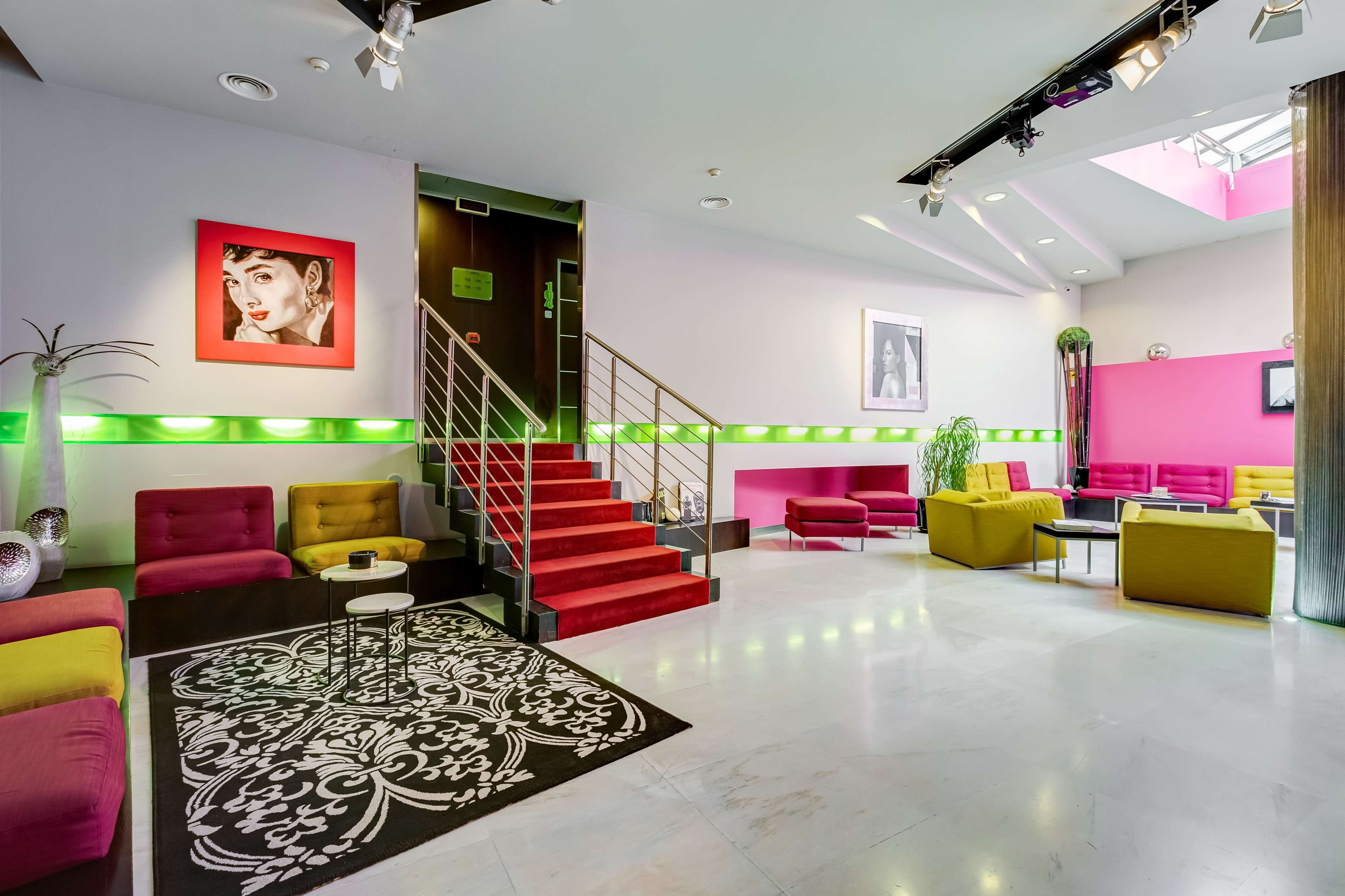 Una hall d'albergo moderna con una scala, posti a sedere rossi e gialli e un tappeto grande con motivi decorativi.