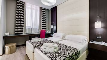 A hotel room with two beds, a desk, a chair, a small stool, a mirror, and a window with curtains.