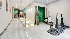 Un hall de hotel con piso de mármol, una escalera, una puerta verde y una exhibición de cactus.
