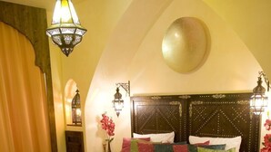 Ein Schlafzimmer mit einem großen Bett, einem gemusterten Überwurf, dekorativen Wandleuchten und einem runden Spiegel an der Wand.