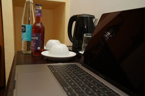 A laptop on a wooden table with a bottle of water, a glass, and a coffee maker. - Hotel Villa Oriental & Restaurant by ANS (Frankfurt)