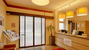 Ein Hotel-Empfangsbereich mit Empfangstresen, einer Pflanze, einem großen Fenster und Blick auf die Stadt.