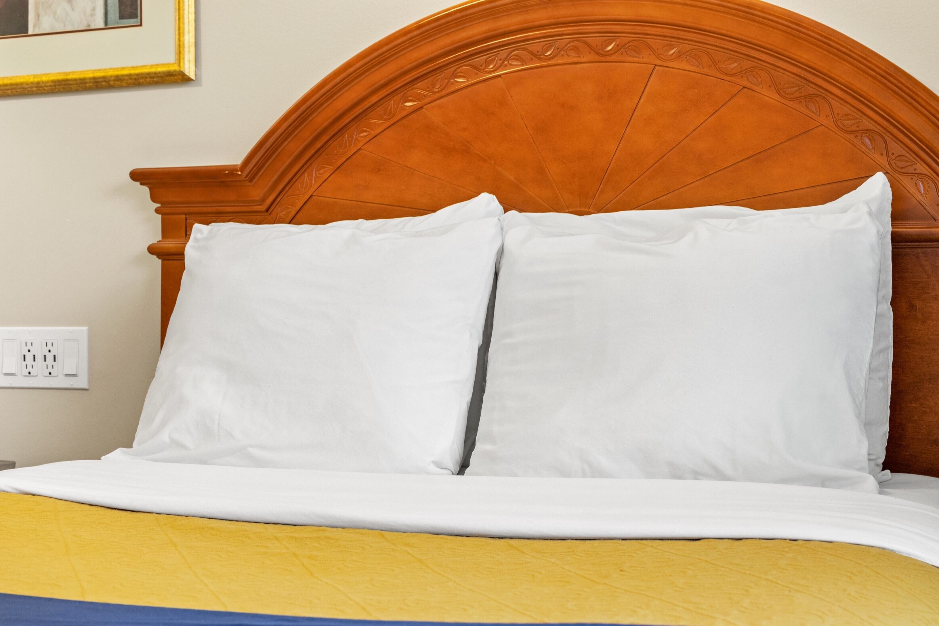 A neatly made bed with white pillows and a yellow and blue bedspread.