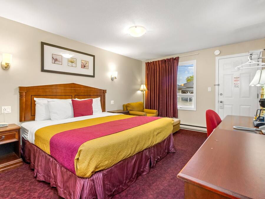 A hotel room with a large bed, a desk, a chair, and a window with curtains.