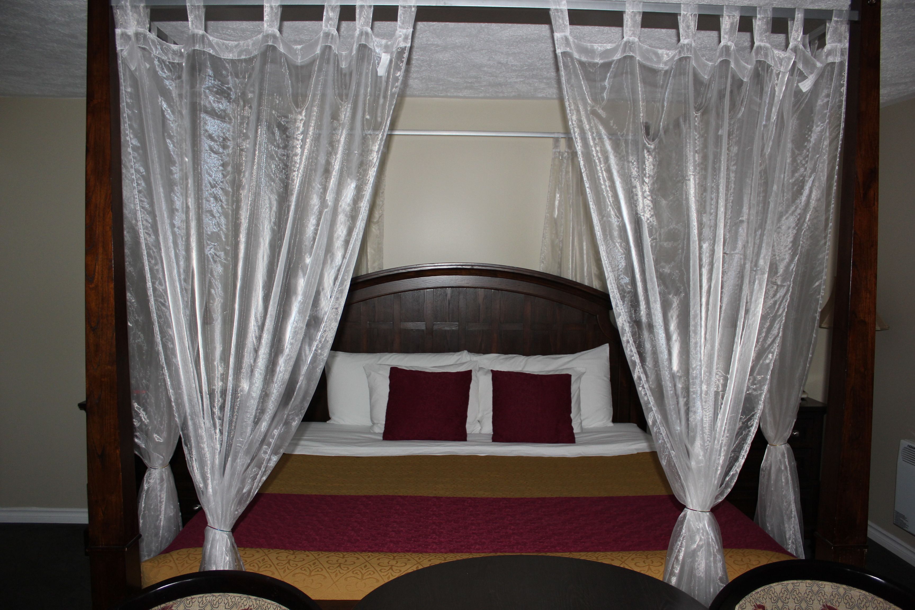 A bed with a canopy, a wooden headboard, and a red bedspread.