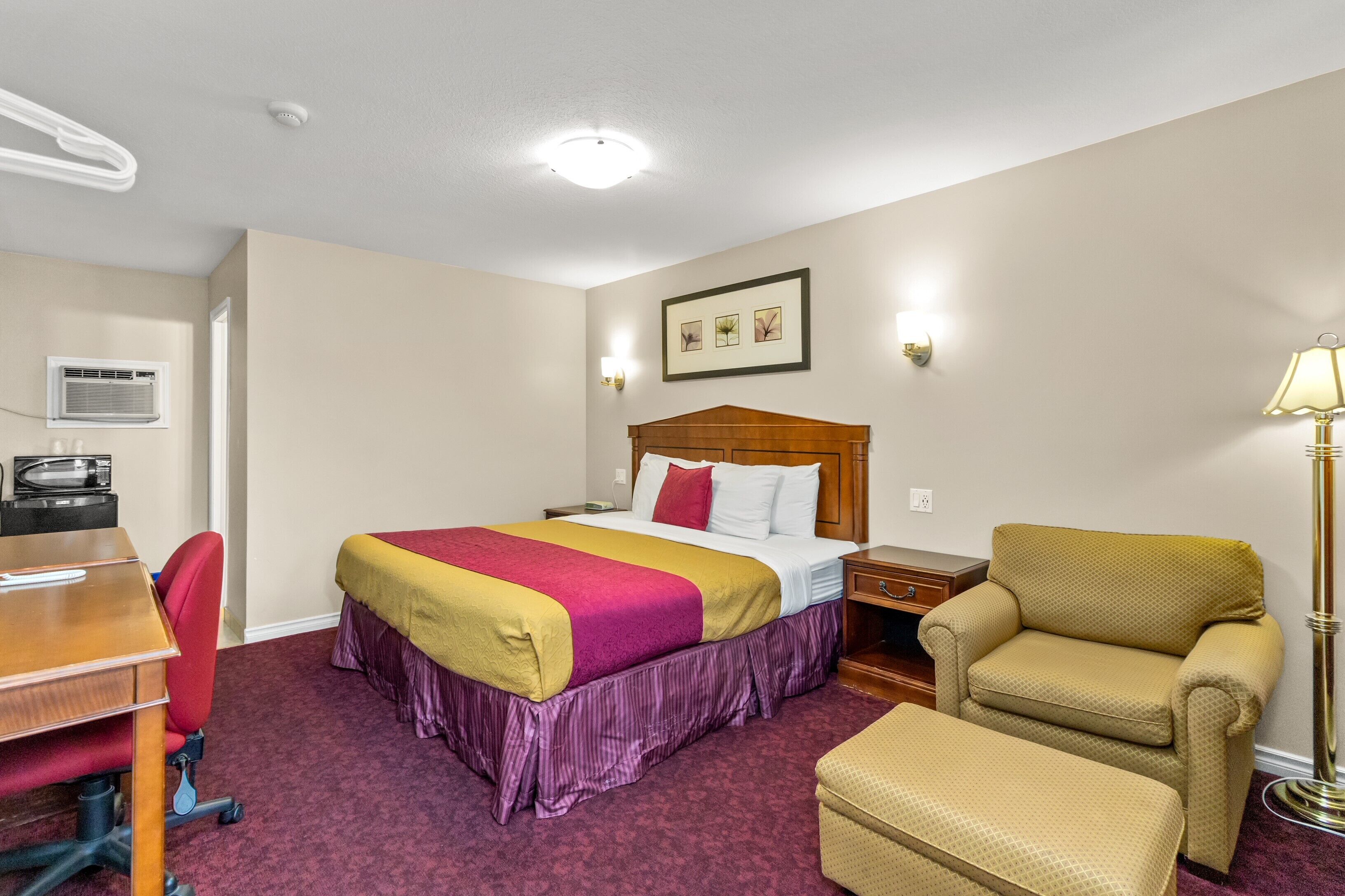 A hotel room with a bed, a desk, a chair, a lamp, and a picture on the wall.
