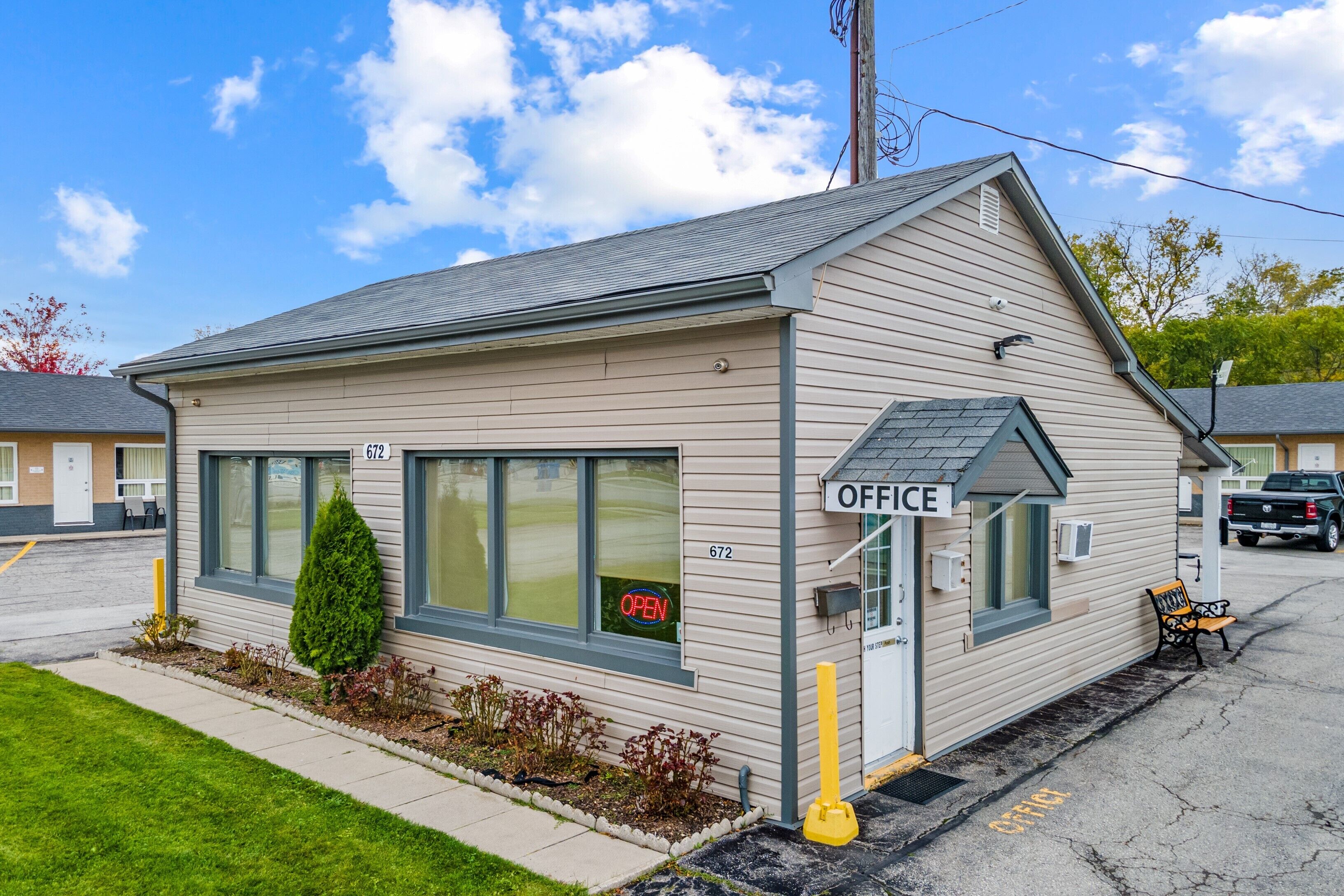 A small, single-story building with a 'OFFICE' sign, numbered 672, and a 'OPEN' sign on the window.