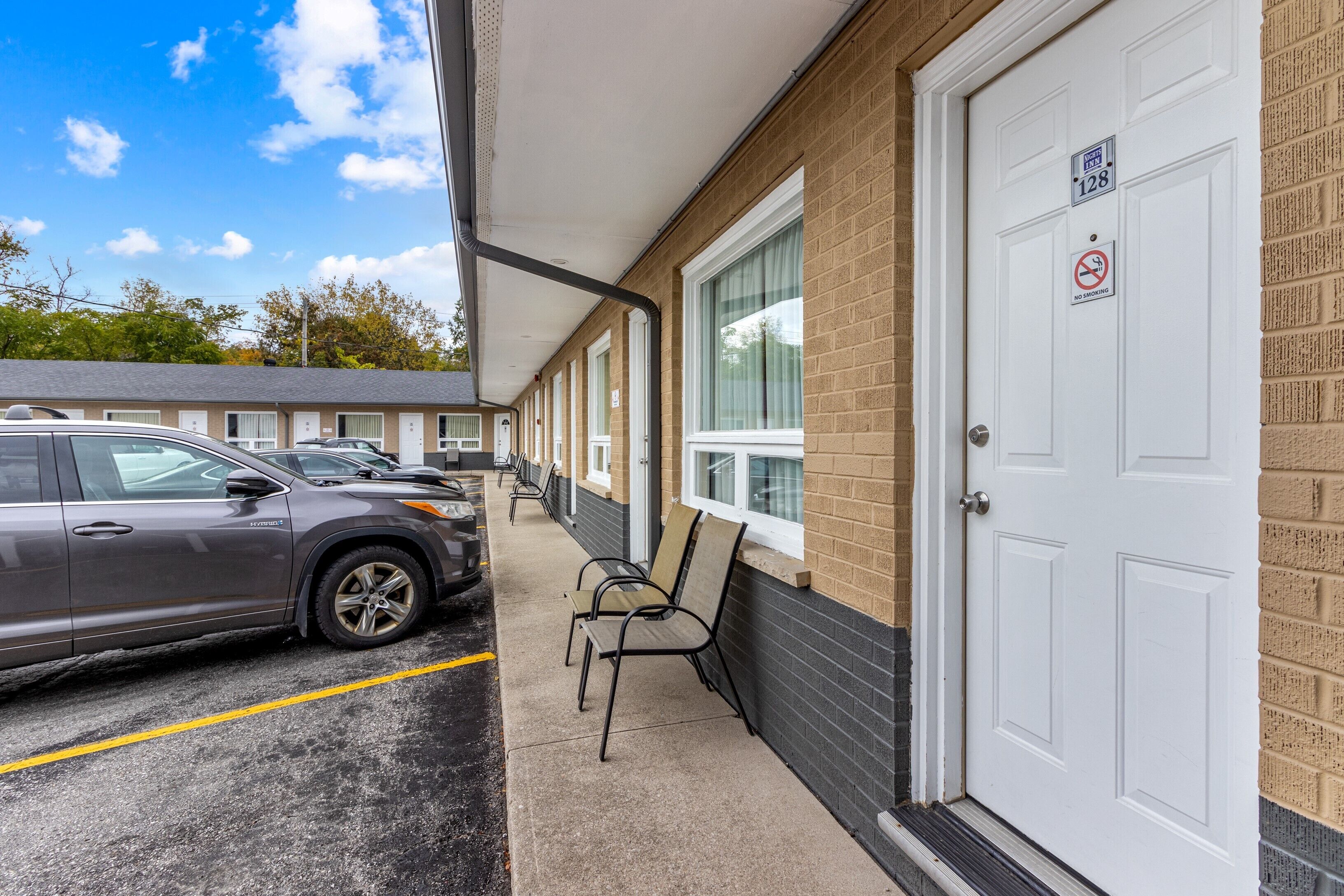A motel with a row of rooms, a covered parking area, and a no smoking sign on the door.