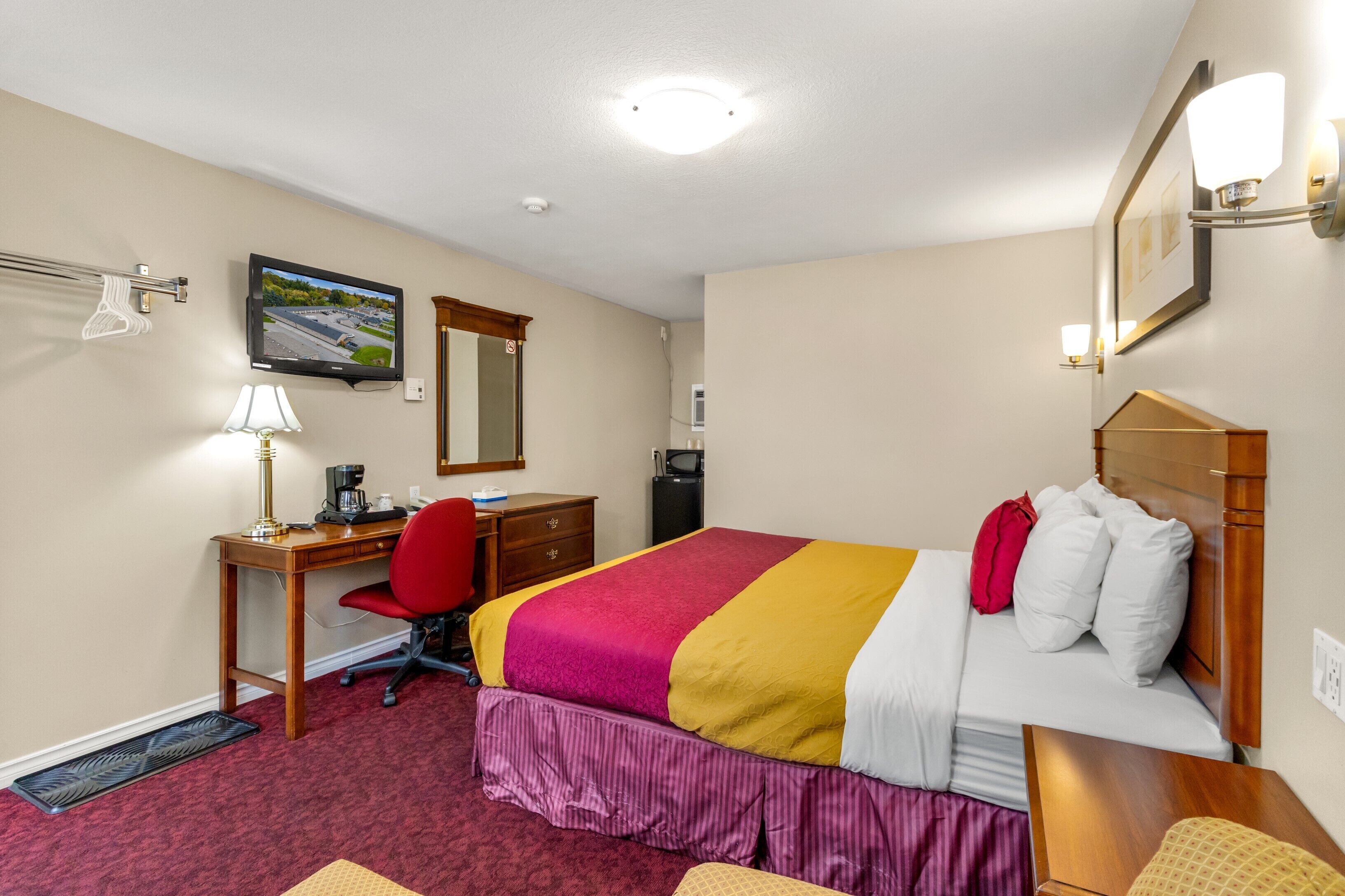 A hotel room with a bed, desk, chair, and a television on the wall.